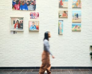 Traveller walking past wall hung with original paintings.