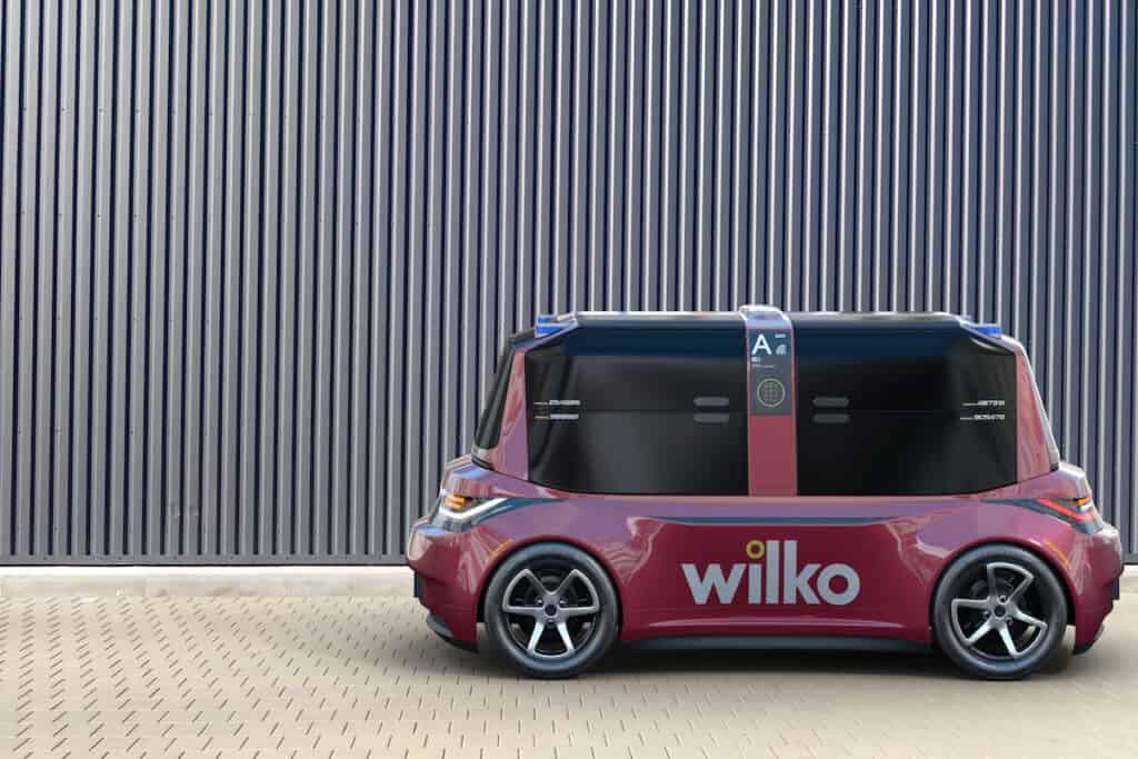 Side view of Pix-E small road-going electric delivery vehicle, pictured Rear view of Pix-E small road-going electric delivery vehicle, pictured in burgundy livery of omnichannel retailer Wilko, against vertical-striped grey fence.
