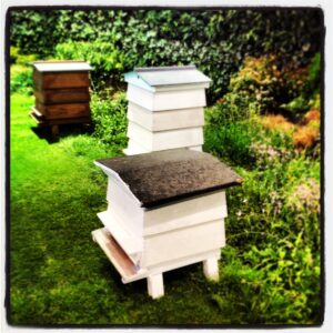 Three different styles of beehive pictured in a garden.