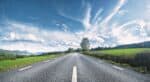 View down a straight empty road, with central white line markings, running into the horizon between fields in Sweden.
