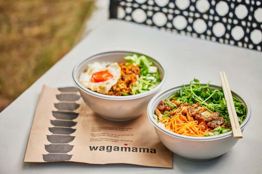 Two new recyclable delivery bowls full of food, with chopsticks across one, plus Wagamama paper below.