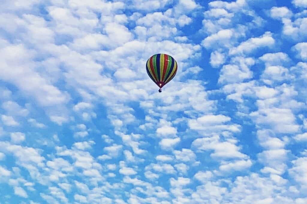 Multi-coloured striped hot air ballon flying high against blue sky covered with cloudlets.