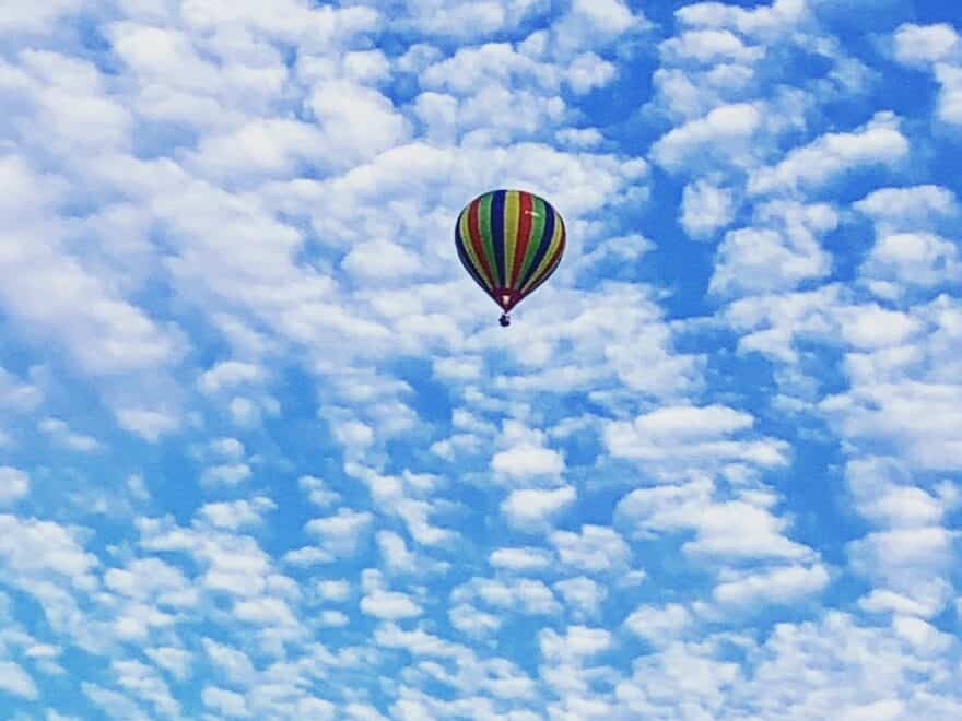 Multi-coloured striped hot air ballon flying high against blue sky covered with cloudlets.