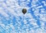 Multi-coloured striped hot air ballon flying high against blue sky covered with cloudlets.