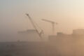 Construction cranes barely visible through smog-like dust cloud.