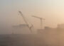 Construction cranes barely visible through smog-like dust cloud.