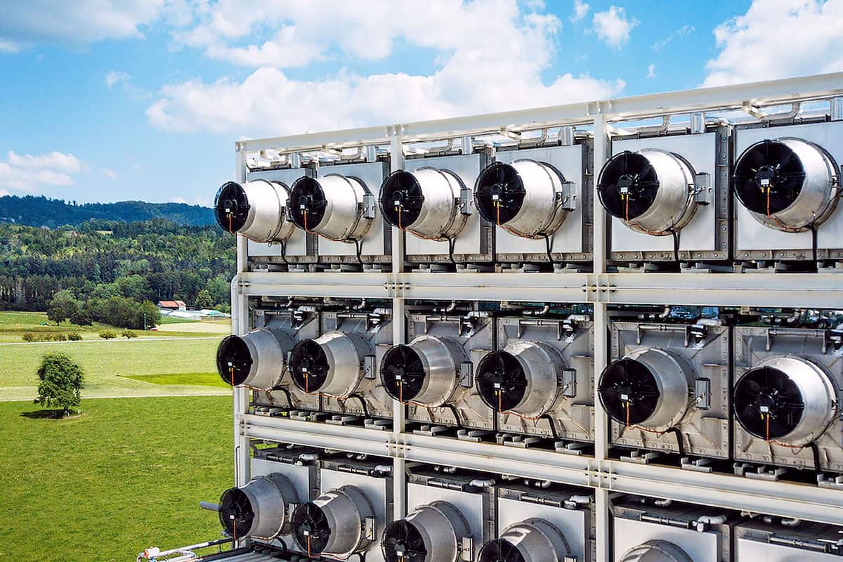 Close-up of Climeworks Direct Air Capture (DAC) plant technology in foreground, with backdrop of Swiss countryside and blue sky.