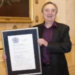 Shaun McCarthy OBE pictured holding a framed certificate on behalf of the Supply Chain Sustainability School, to commemorate receipt of the Queen's Award for Enterprise, in 2022.