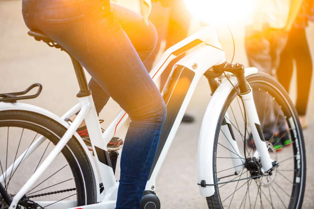 Close up of battery pack of a modern, white electric bicycle, being ridden by person wearing blue jeans, with legs only visible.