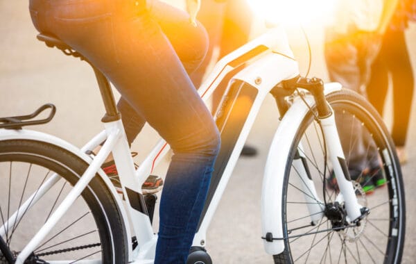 Close up of battery pack of a modern, white electric bicycle, being ridden by person wearing blue jeans, with legs only visible.