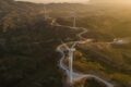 Aerial shot of wind turbines dotted along winding road through beautiful rural landscape.
