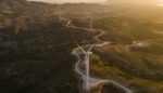 Aerial shot of wind turbines dotted along winding road through beautiful rural landscape.
