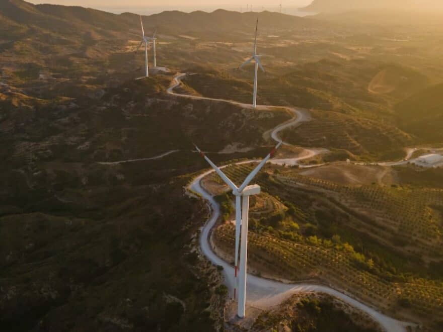 Aerial shot of wind turbines dotted along winding road through beautiful rural landscape.