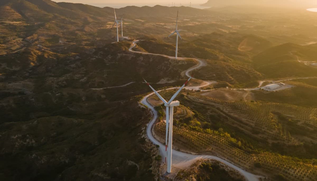 Aerial shot of wind turbines dotted along winding road through beautiful rural landscape.