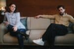 Stars Rose Leslie and Kit Harington pictured in still from the film, seated looking unhappy at opposite ends of settee.