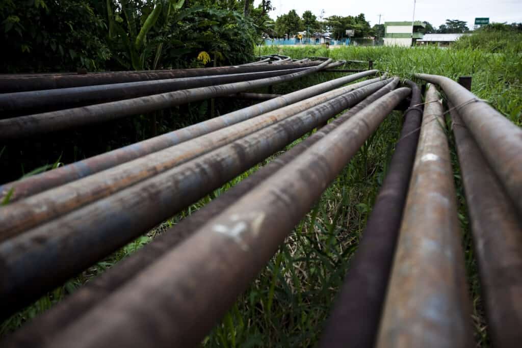 Multiple rusty oil pipelines heading into the distance across green grass.