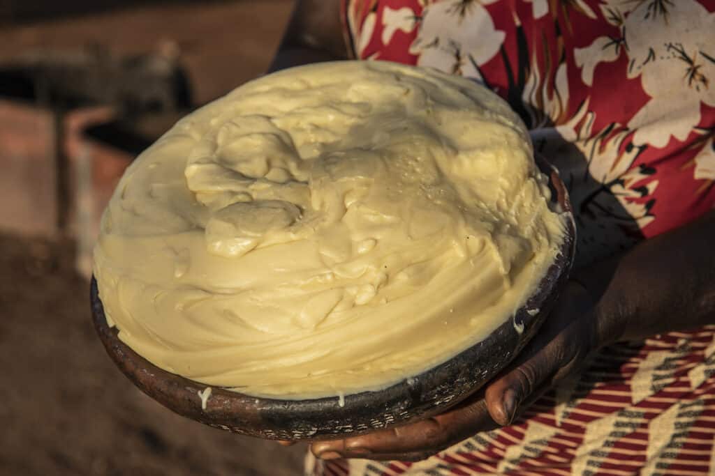 Bowl of yellow custard-like shea butter being held up to see. Photo credit: Makke Hussein.