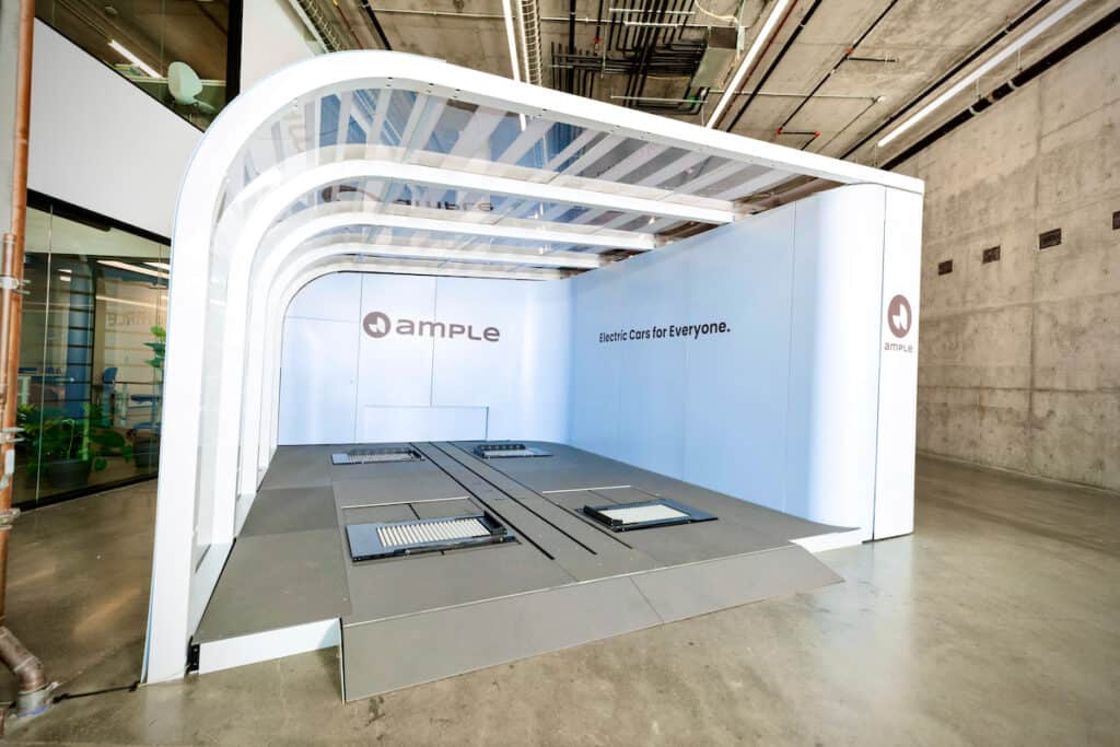 Ample battery swapping station in white — an open garage-like bay, with company logo on back wall and 'Electric Cars for Everyone' inside on right.