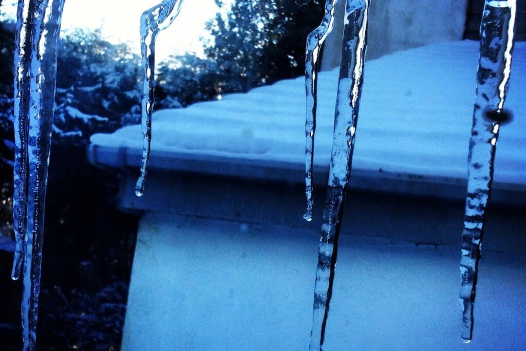 Icicles hanging down blue-filtered view out over snow-covered roof.