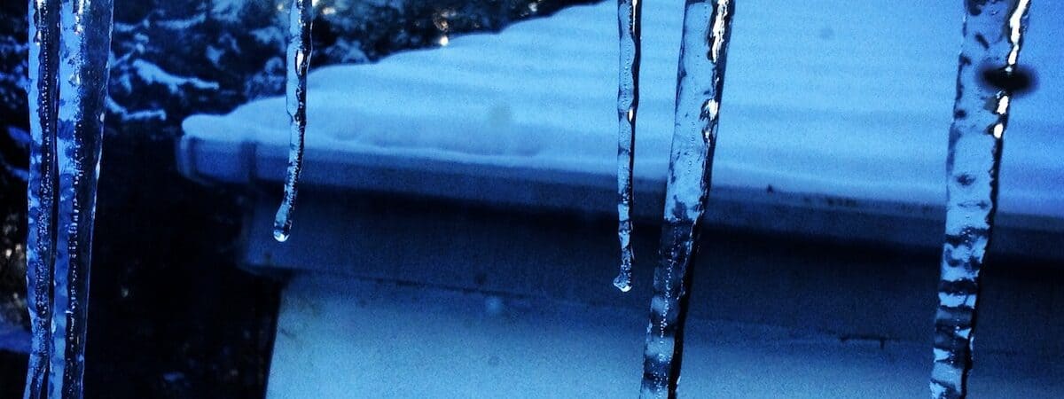 Icicles hanging down blue-filtered view out over snow-covered roof.