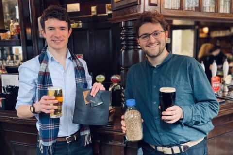 Arda Founders Edward TJ Mitchell and Brett Cotten pictured in pub holding glasses of beer, sample of leather alternative and bottle of spent grain.