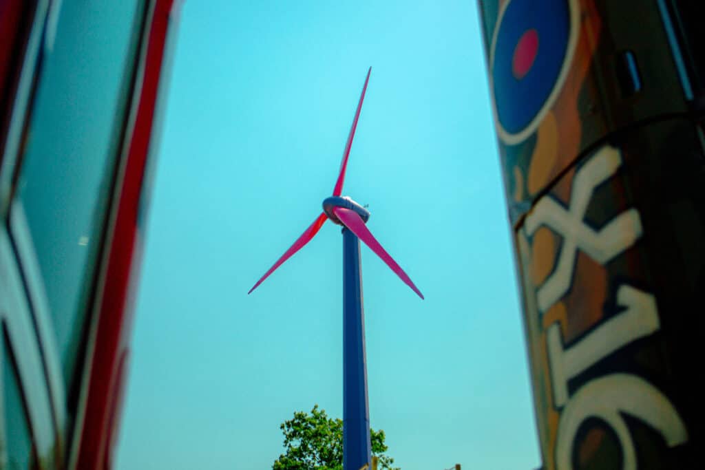 Pink blades on top of purple wind turbine pictured against bright blue sky.