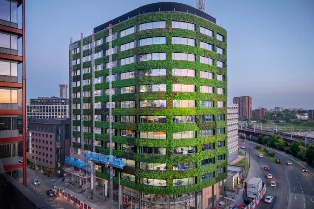 12-storey Eden building on city-centre corner site at dusk, with living wall giving green façade between windows from 1st-floor upwards.