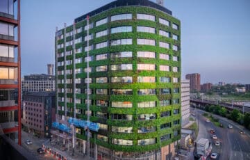 12-storey Eden building on city-centre corner site at dusk, with living wall giving green façade between windows from 1st-floor upwards.