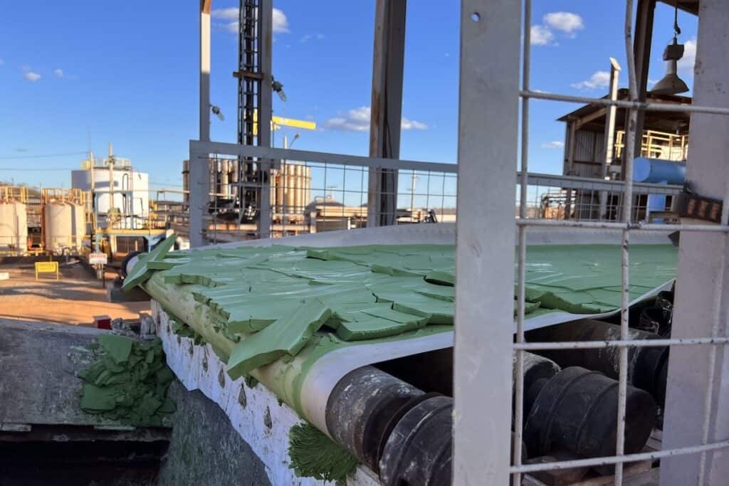 Brazilian Nickel’s site at Piauí, north east Brazil, showing green-coloured minerals on conveyor belt in foreground, with industrial buildings behind.