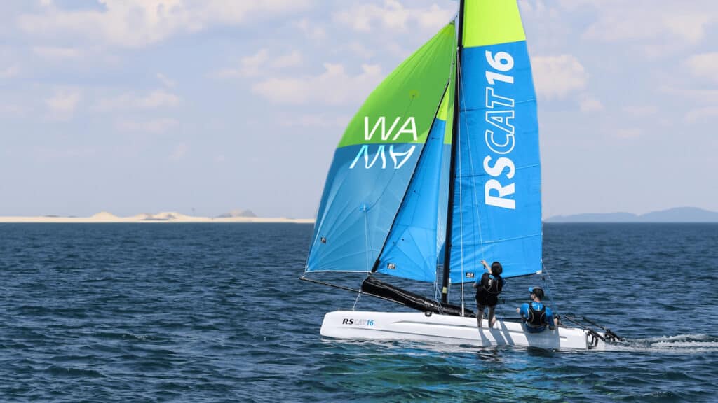 Racing catamaran on open sea with two crew, plus blue and green sails marked RSCAT16.
