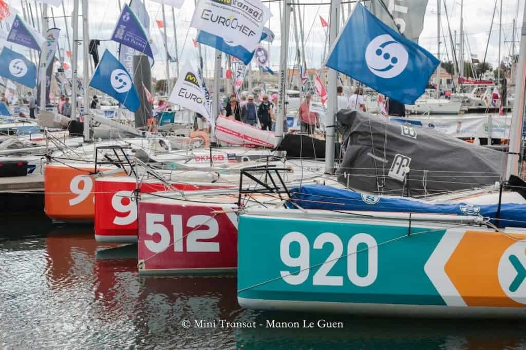 Sailing boats moored close together in marina, shot on diagonal with white three-figure race numbers visible on bright coloured bows.