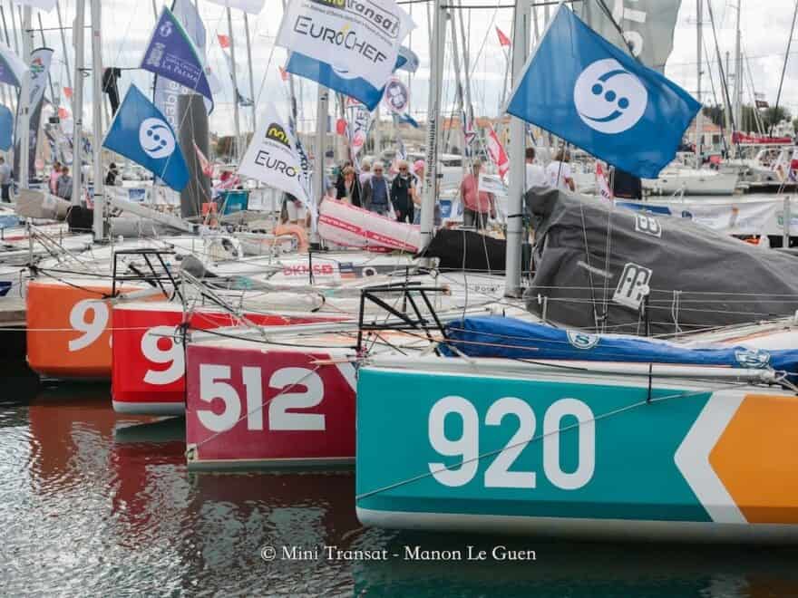 Sailing boats moored close together in marina, shot on diagonal with white three-figure race numbers visible on bright coloured bows.