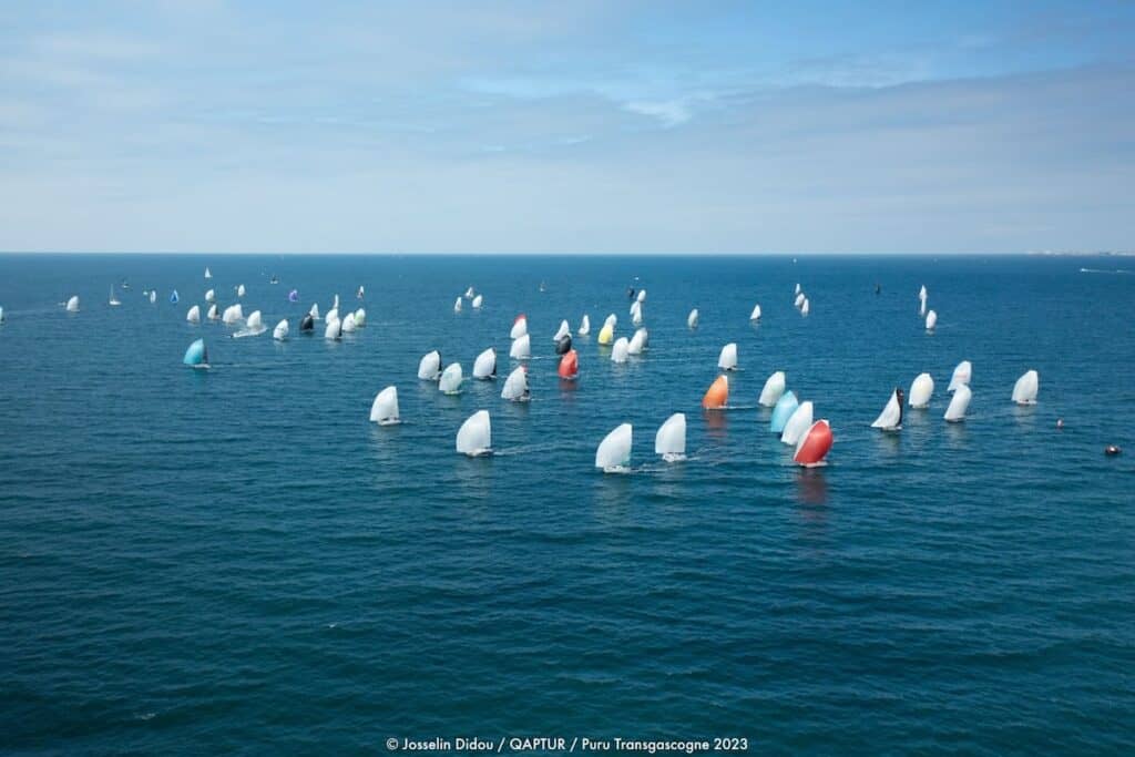 Dozens of racing sail boats viewed from distance and above, on blue sea.
