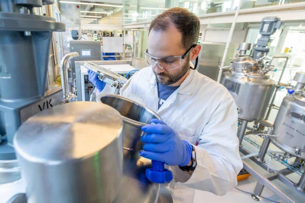 Image of MicroHarvest lab and pilot plant in operation shows person in white coat with blue gloves checking steel production equipment.