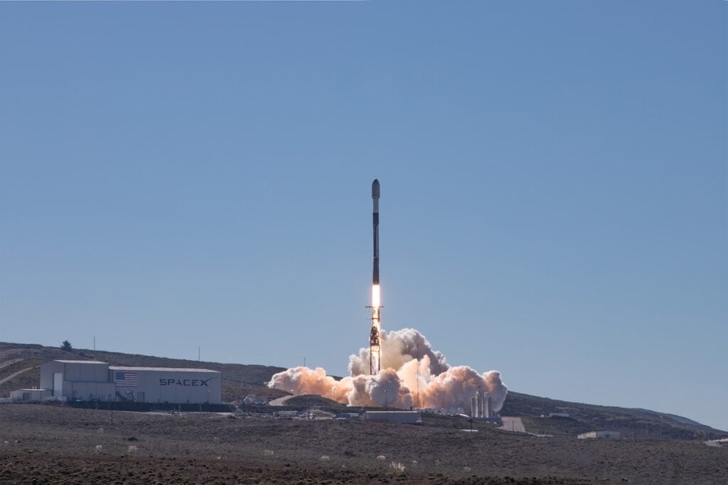 Rocket shown launching alongside building bearing SpaceX branding.