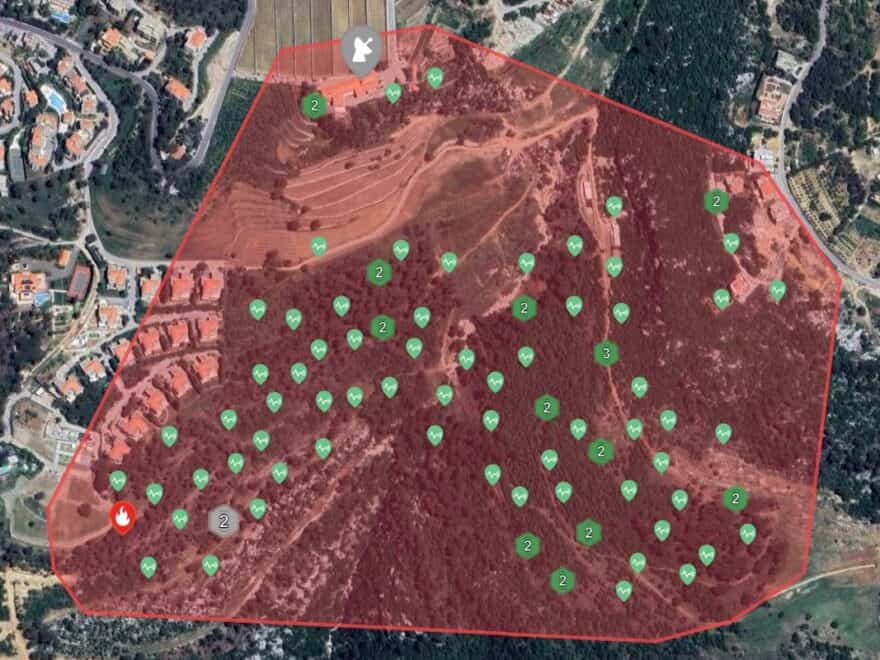 Aerial view of pilot site — wooded central area and residential surrounds, with red and green graphic overlay to indicate source of fire alert.