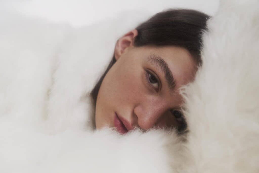 Face of dark-haired model peeking out of fluffy white material.