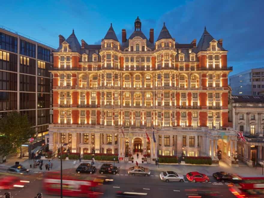 Front elevation of Mandarin Oriental Hyde Park hotel in London, illuminated at twilight, with red London bus and black cab taxis in foreground.