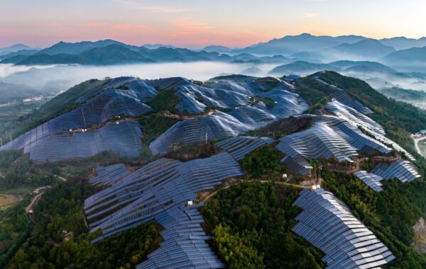 Multiple solar arrays cover woodland hilltops, with mountains in distance.