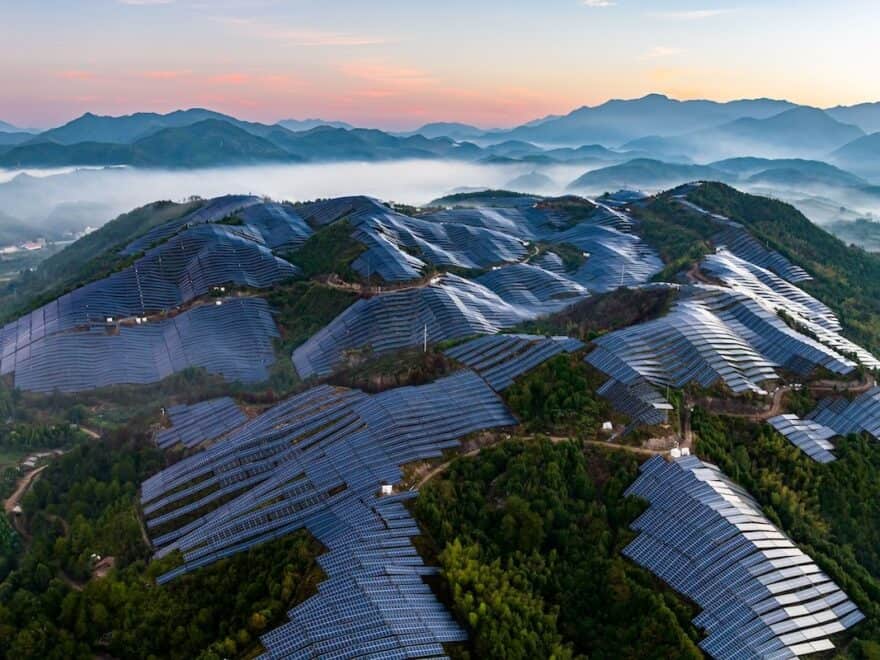 Multiple solar arrays cover woodland hilltops, with mountains in distance.