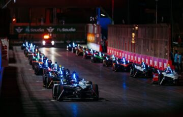 Night shot of Formal E racing cars lined up in two columns on start grid.