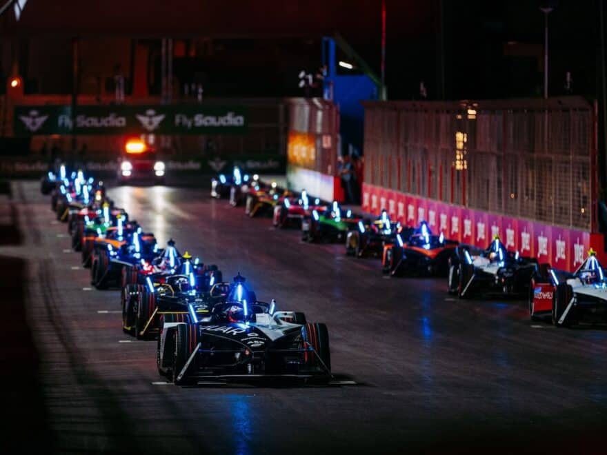 Night shot of Formal E racing cars lined up in two columns on start grid.
