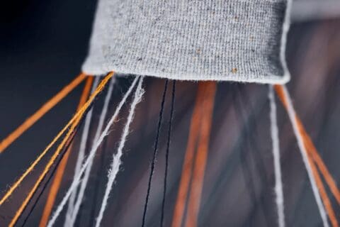 Close-up of orange and grey threads strung out of garment fragment.