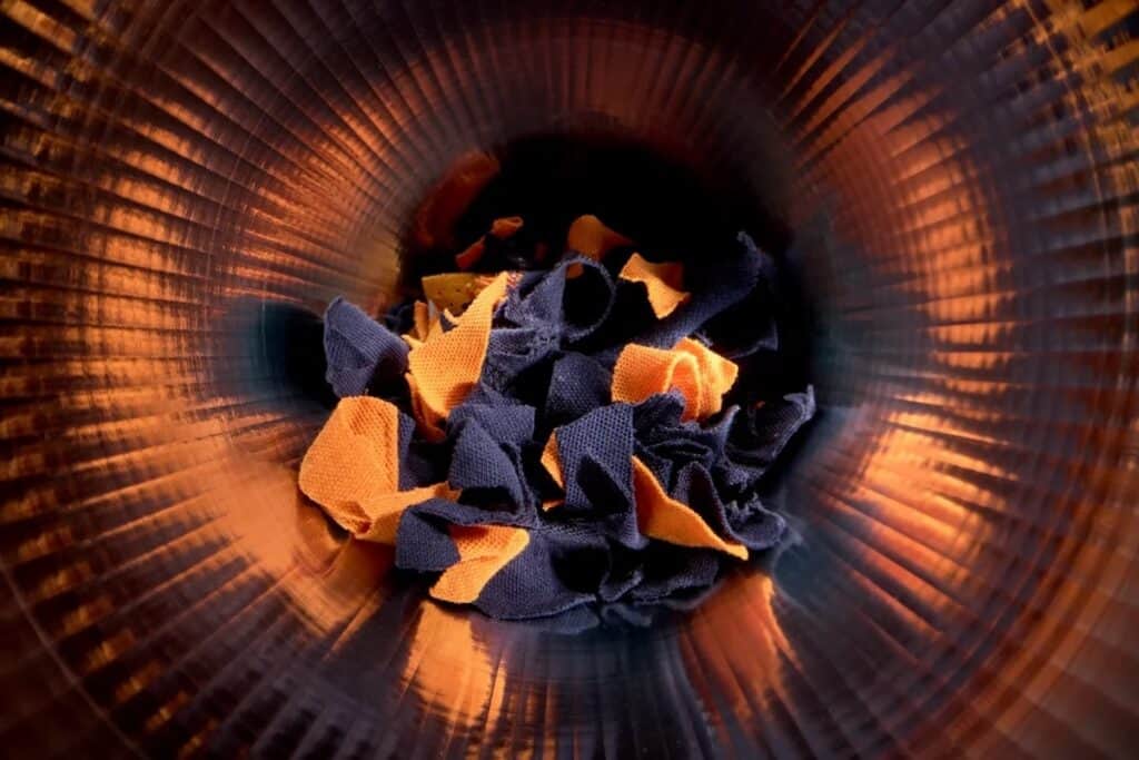 Bundle of orange and blue garment fragments in tumbler-style drum.