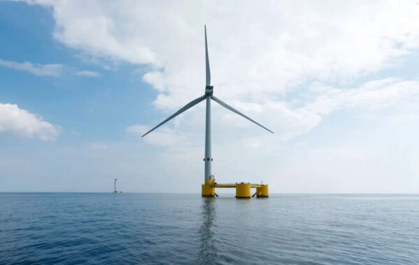 Offshore wind turbine floating out at sea on three-column yellow platform.