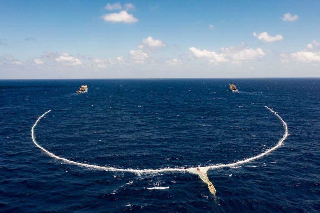 Large barricade deployed in ocean in a loop behind two ships, strung from one to another.