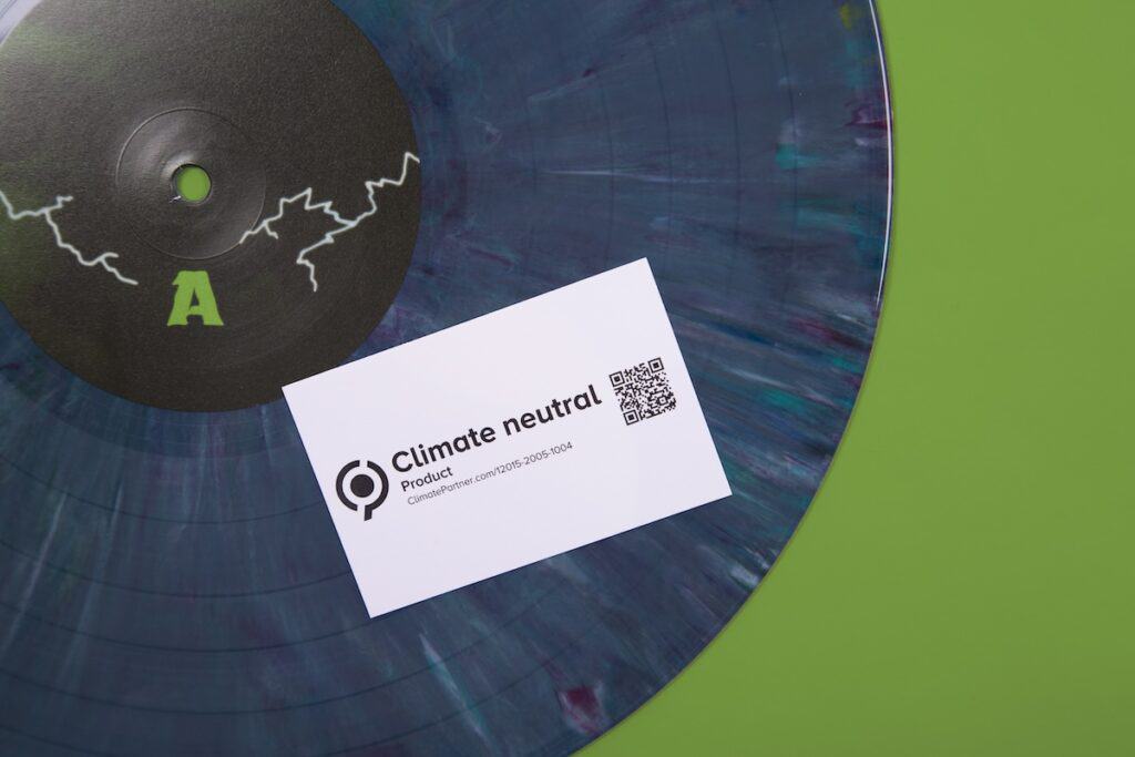 Variegated blue vinyl record, with white card stating 'Climate neutral product' on top, pictured against green background.