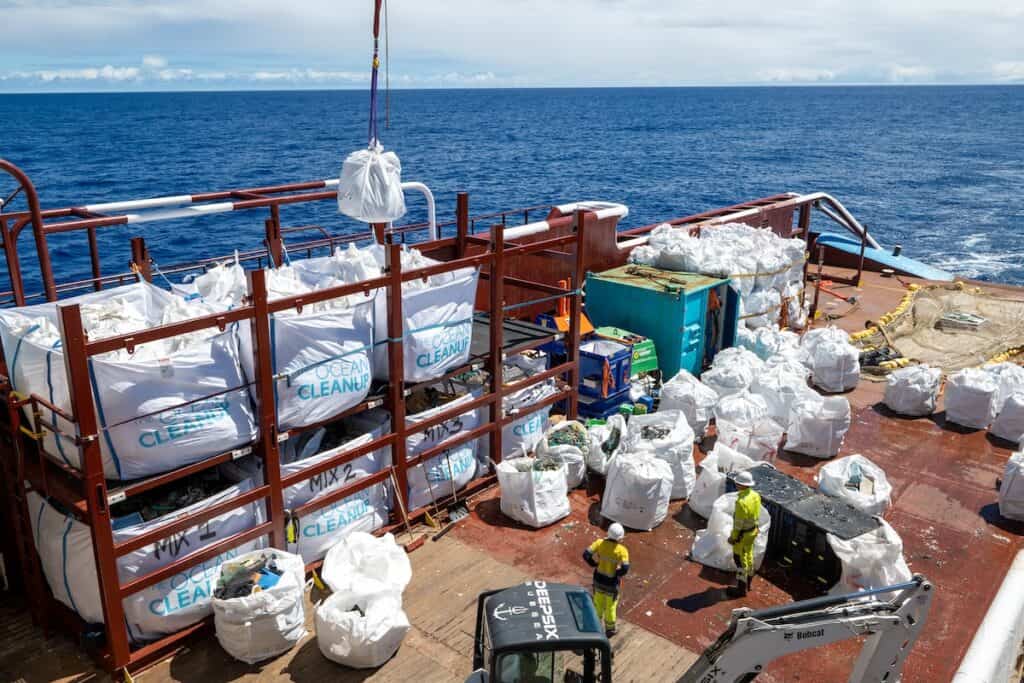 Large white bags of extracted waste being sorted and stored on board deck of ship, with crane shown hoisting some more into place.