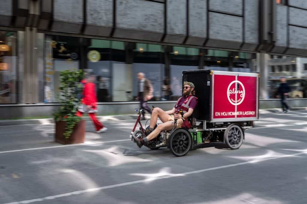Four-wheel Pling cargo bike on street, with delivery driver up front.