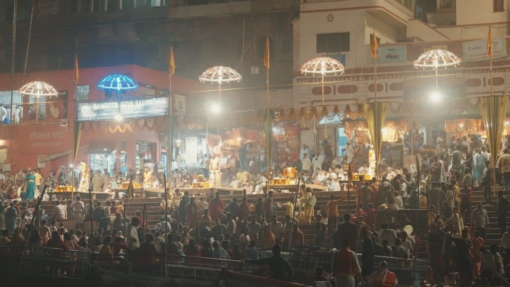 Festival crowds on banks of Ganges River at night, with illuminated parasols above.